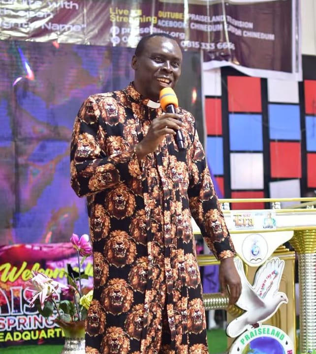 Apostle Prof. E. C. Ejiofor smiling with microphone in hand, wearing a lion-print robe at the altar