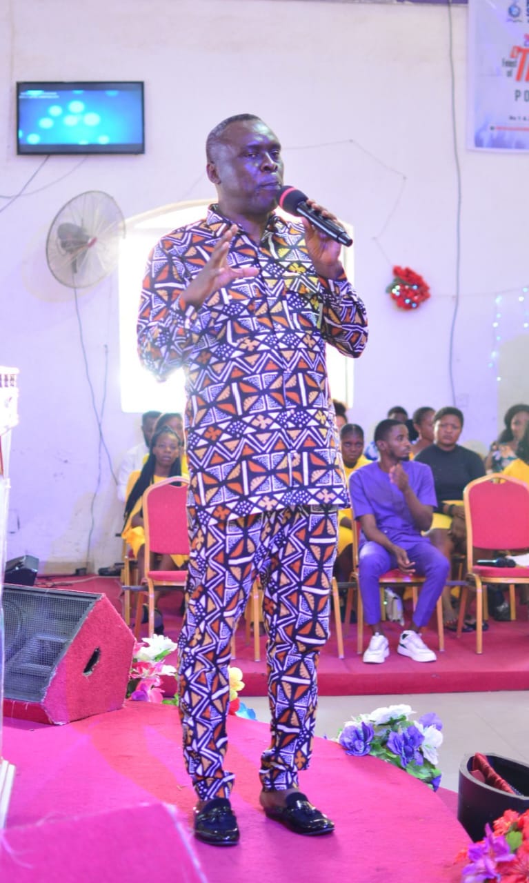 Apostle Prof. E. C. Ejiofor preaching in a vibrant patterned outfit, holding a microphone at Praiseland Royal Springs Int'l Church