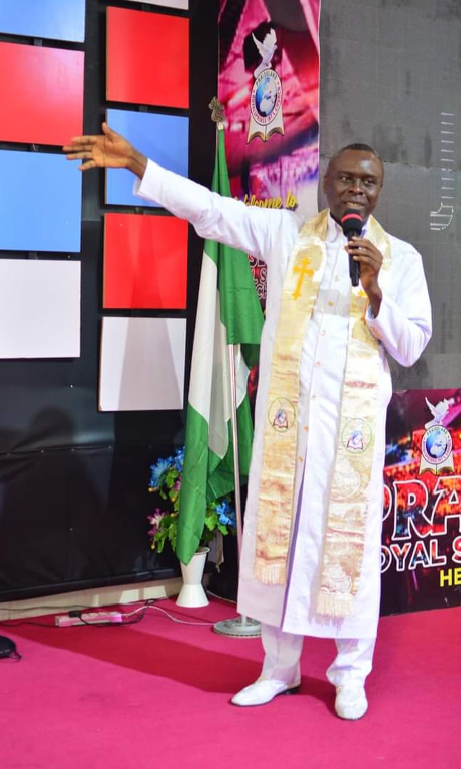Apostle Prof. E. C. Ejiofor ministering with a microphone, wearing a white robe with a cream stole embroidered with a gold cross