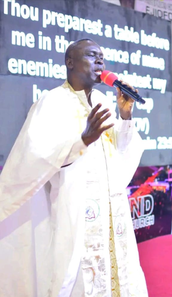 Apostle Prof. E. C. Ejiofor ministering with a microphone in a white robe with an embroidered stole