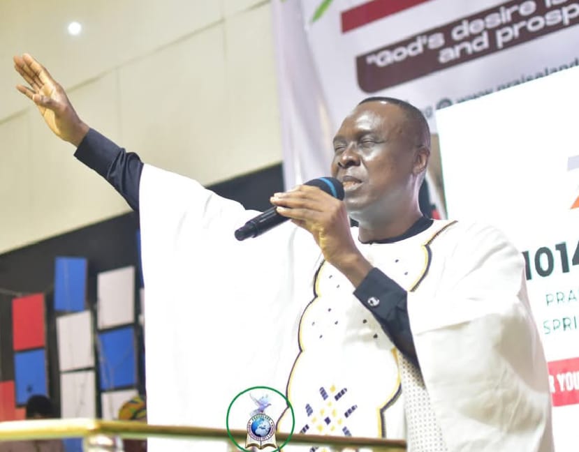 Apostle Prof. E. C. Ejiofor preaching in a white robe with decorative embroidery at Praiseland Royal Springs Int'l Church