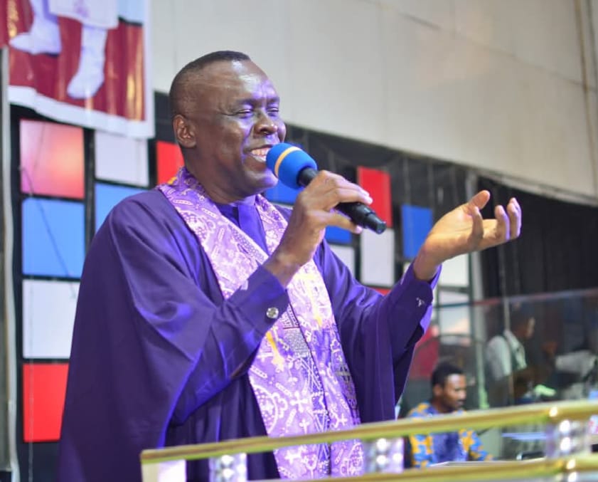 Apostle Prof. E. C. Ejiofor ministering with a microphone in a purple robe and embroidered stole