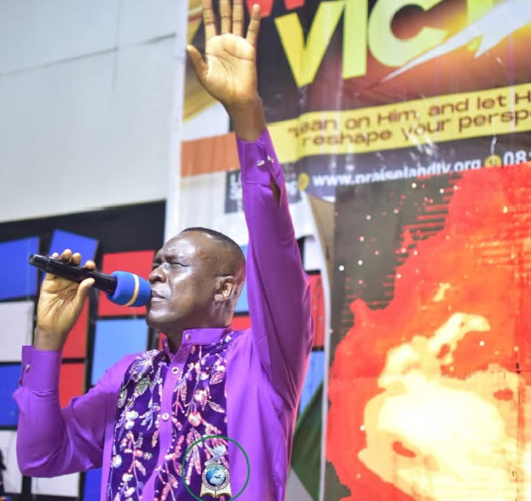 Apostle Prof. E. C. Ejiofor preaching in a purple embroidered robe, holding a microphone with one hand raised at Praiseland Royal Springs Int'l Church