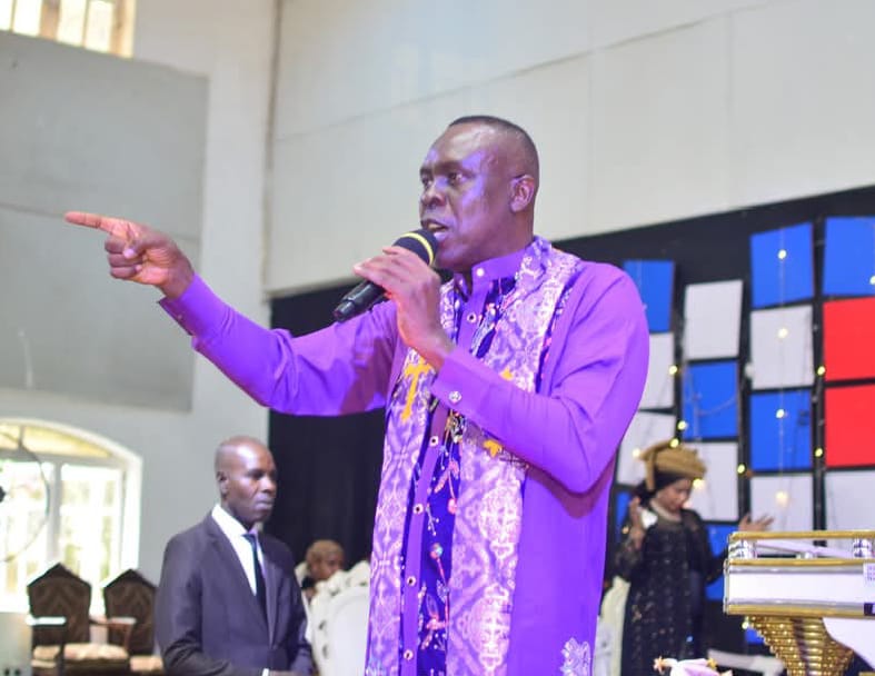Apostle Prof. E. C. Ejiofor preaching with a microphone, wearing a purple robe and a patterned purple stole