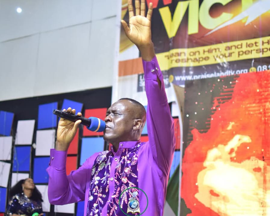 Apostle Prof. E. C. Ejiofor preaching in a purple embroidered robe with raised hand at Praiseland Royal Springs Int'l Church