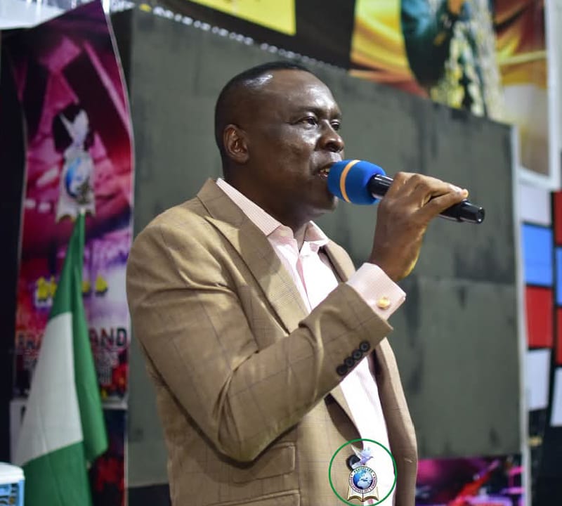 Apostle Prof. E. C. Ejiofor preaching in a tan suit at Praiseland Royal Springs Int'l Church