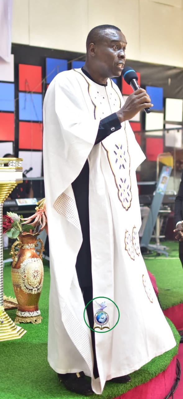 Apostle Prof. E. C. Ejiofor ministering with a microphone in a white and black embroidered robe